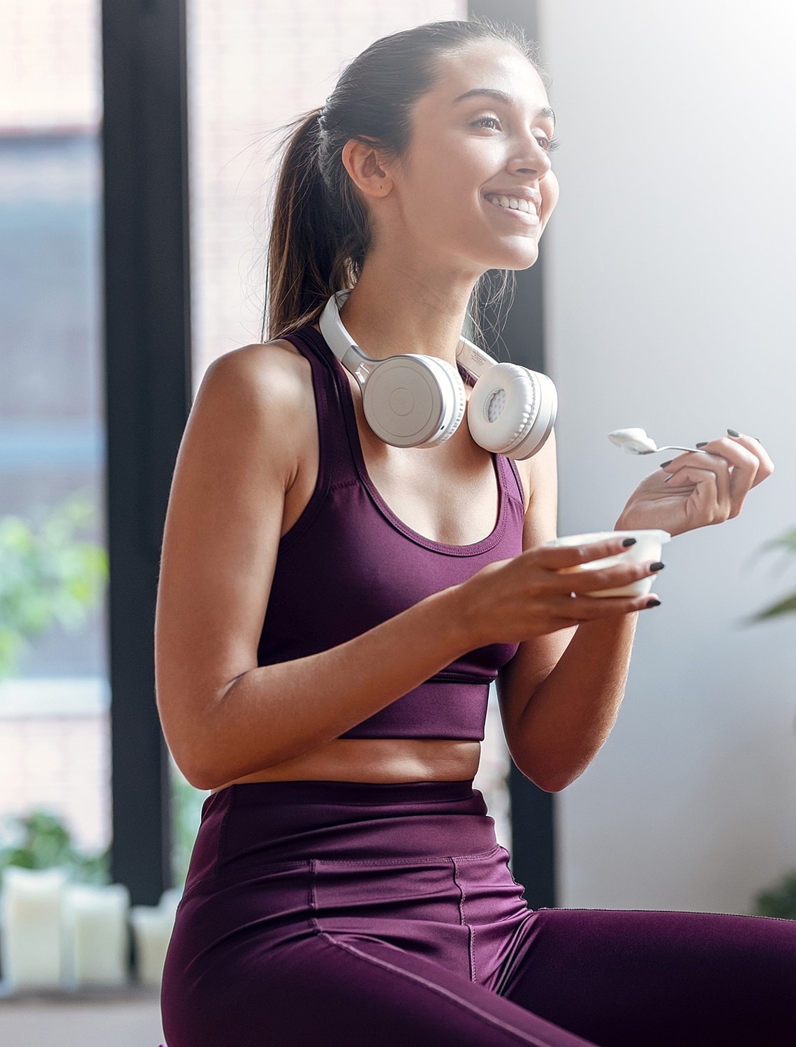 Smiling woman enjoying yogurt with headphones on.