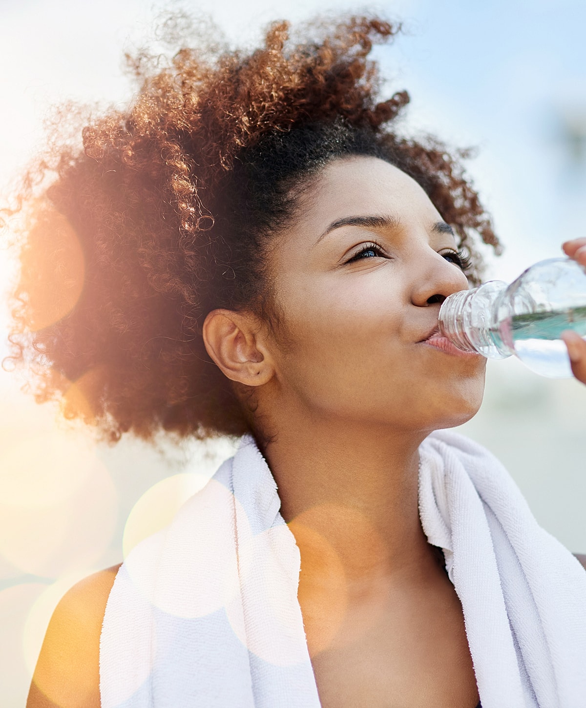 Woman drinking water after exercising outdoors.