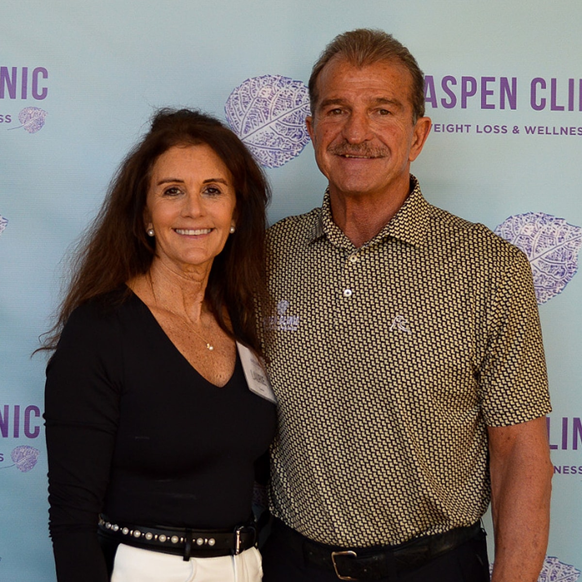Couple posing at Aspen Clinic event backdrop.