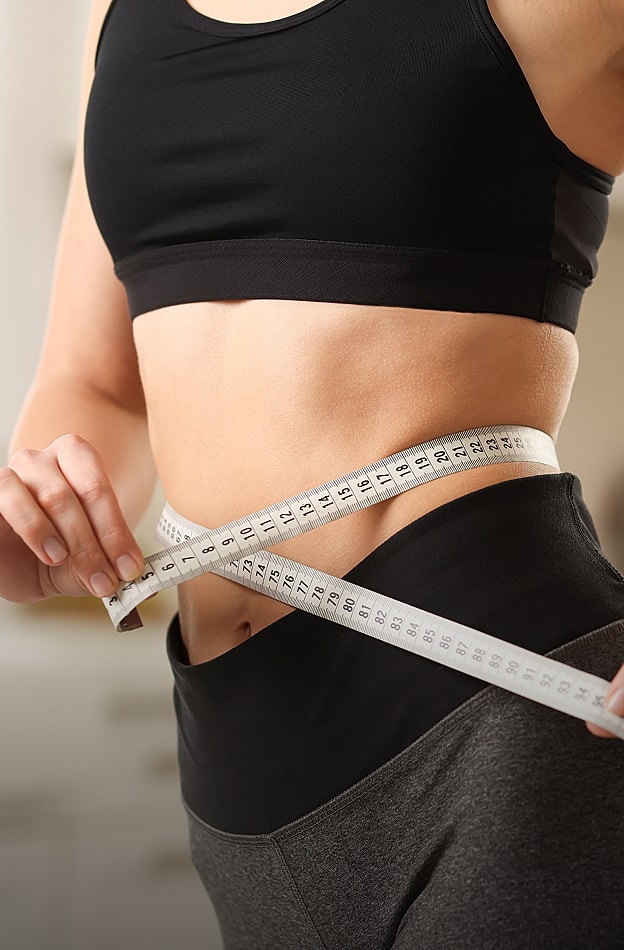 Person measuring waist with tape measure.