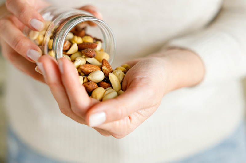 Woman pouring mixed nuts out of glass jar 